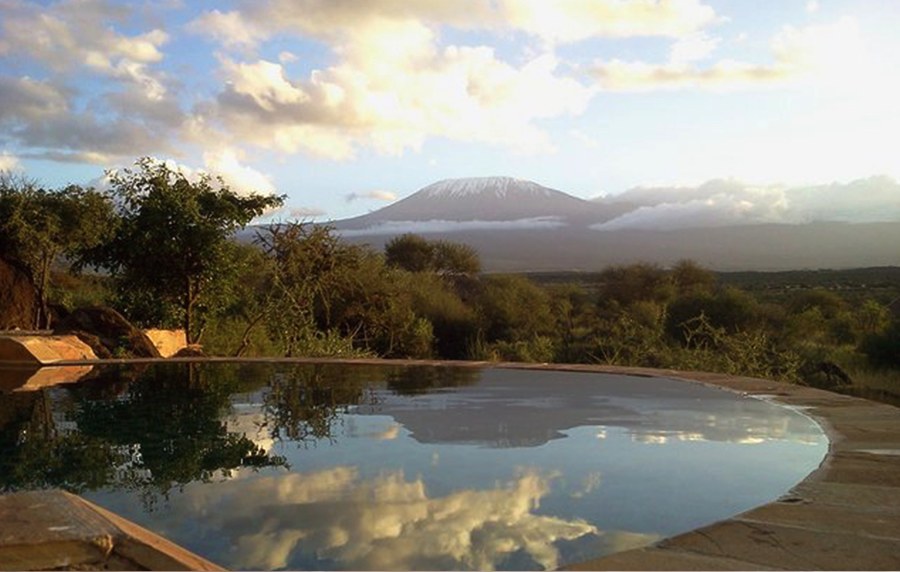 Pool at Satao Elerai reflecting clouds, with bush and snow-capped Kilimanjaro in the distance
