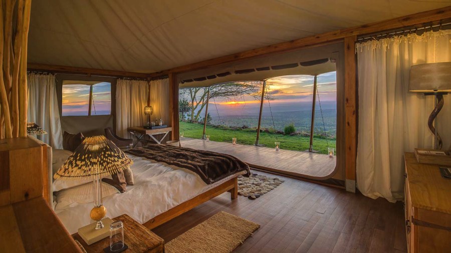 Tent at Elewana Loisaba Tented Camp with a bed facing open doors, a deck and the valley at sunset
