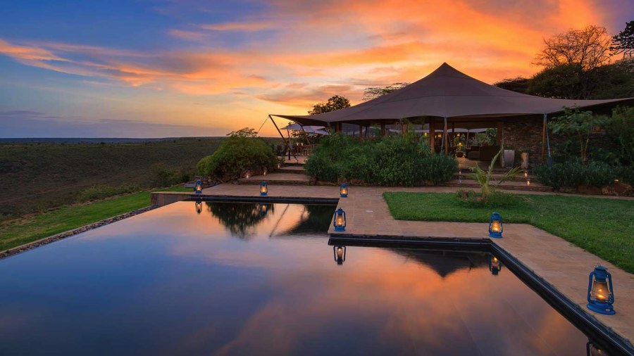 Pool lined with lanterns at Elewana Loisaba Tented Camp, reflecting the main tent and an orange sunset