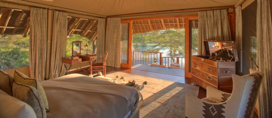 Tented suite at Finch Hattons with a bed, writing desk, armchair and open doors to a deck over the water