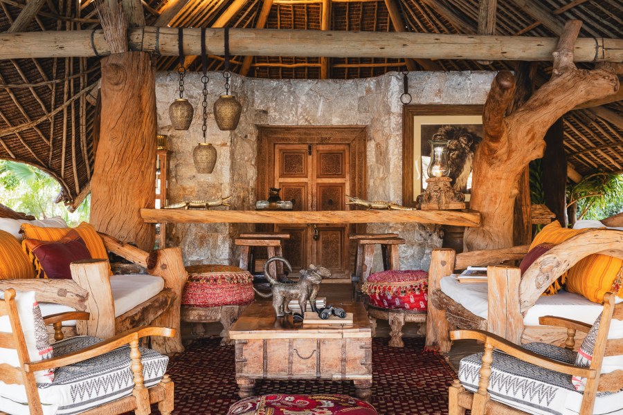Lounge at Galdessa Camp with driftwood furniture, a stone wall, carved doors and a thatched roof