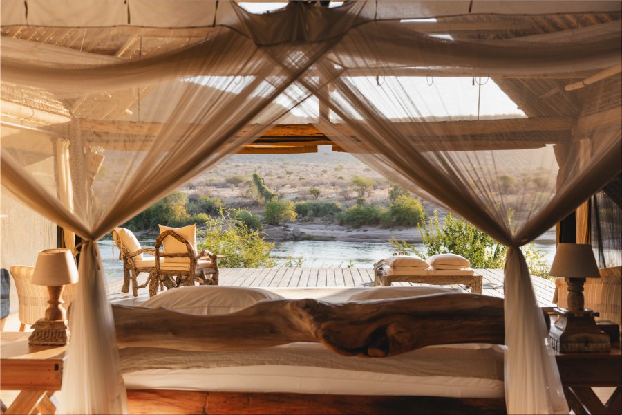 View from a netted bed at Galdessa Camp across a deck with chairs to the Galana River