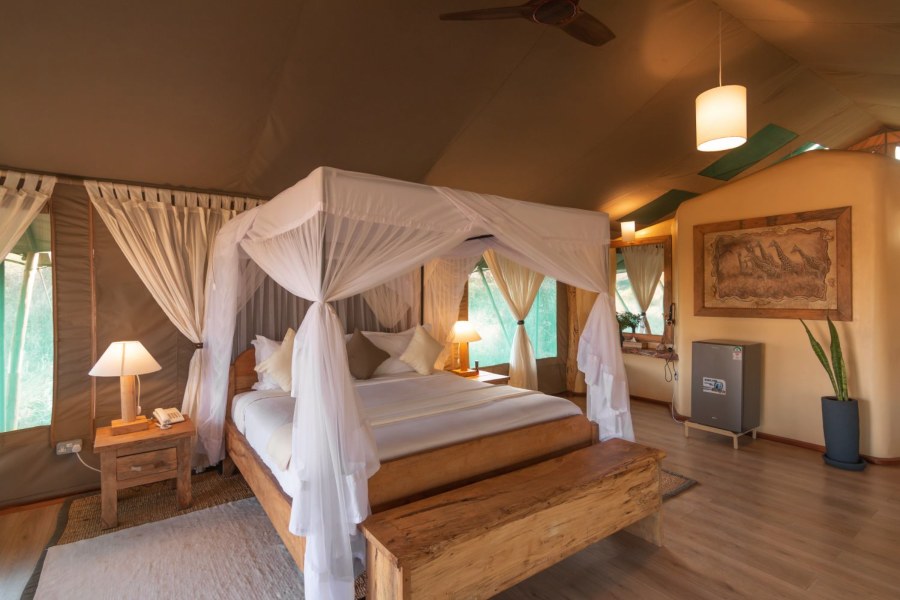 Tent interior at Kibo Safari Camp with a canopy bed draped in white netting and a carved giraffe panel on the wall
