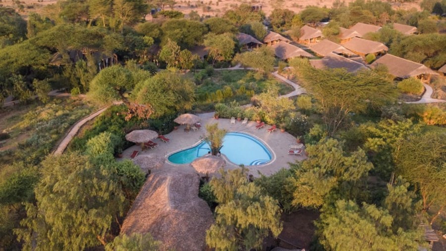 Aerial view of Kibo Safari Camp near Amboseli, with thatched tents and a swimming pool among green trees