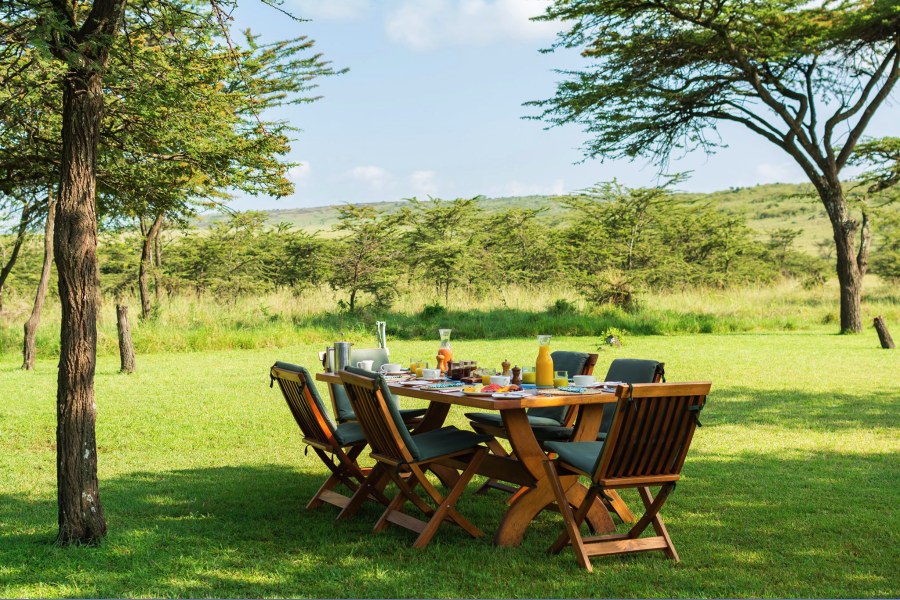 Breakfast table set on the lawn under acacia trees at Kicheche Bush Olare in the Olare Motorogi Conservancy