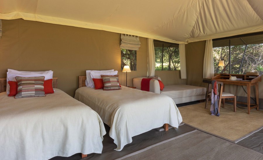 Twin beds with red cushions, a daybed and a writing desk inside a tent at Kicheche Mara North