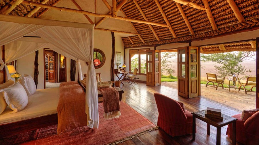 Thatched cottage bedroom with a canopy bed and doors open to a terrace at Elewana Kifaru House on Lewa