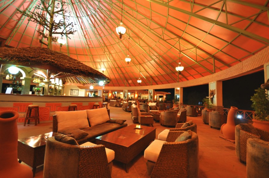 Lounge and bar under a high domed roof at Kilima Safari Camp, with wicker sofas and armchairs lit at night