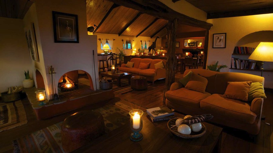Lounge with sofas, a lit fireplace, bookshelves and candles at Elewana Lewa Safari Camp in the evening