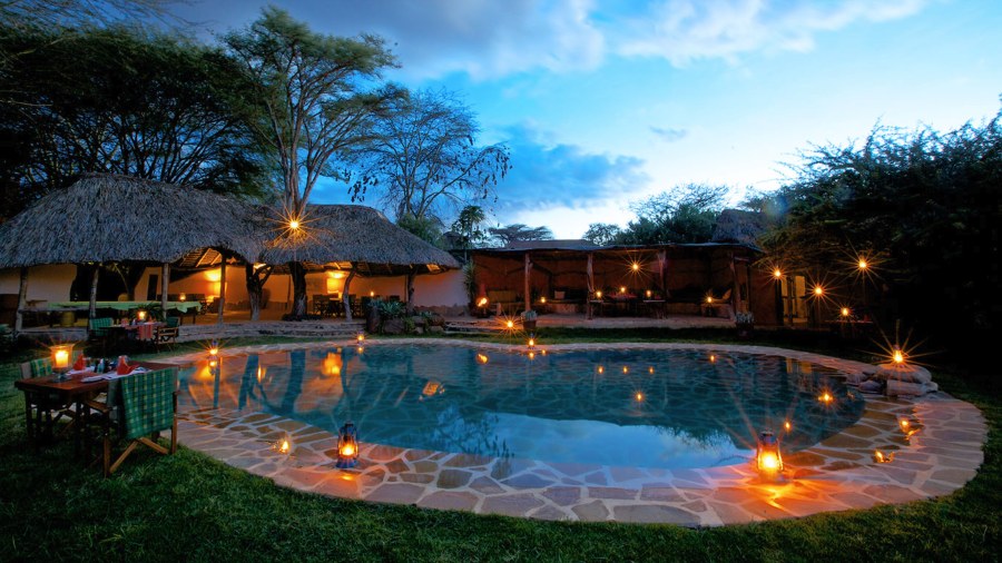 Swimming pool ringed by lanterns in front of thatched buildings at Elewana Lewa Safari Camp at dusk