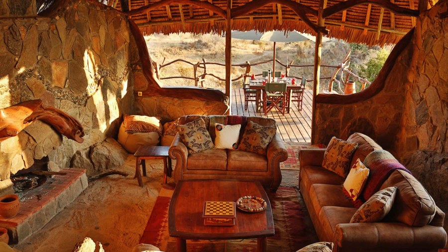 Stone-walled lounge with leather sofas and a fire pit at Loisaba Star Beds, opening onto a deck with a dining table