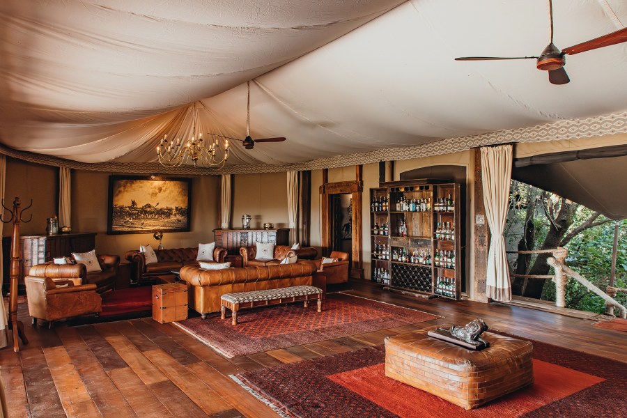 Lounge tent at Mara Plains Camp with leather sofas, a chandelier, a drinks cabinet and red rugs on wooden floors