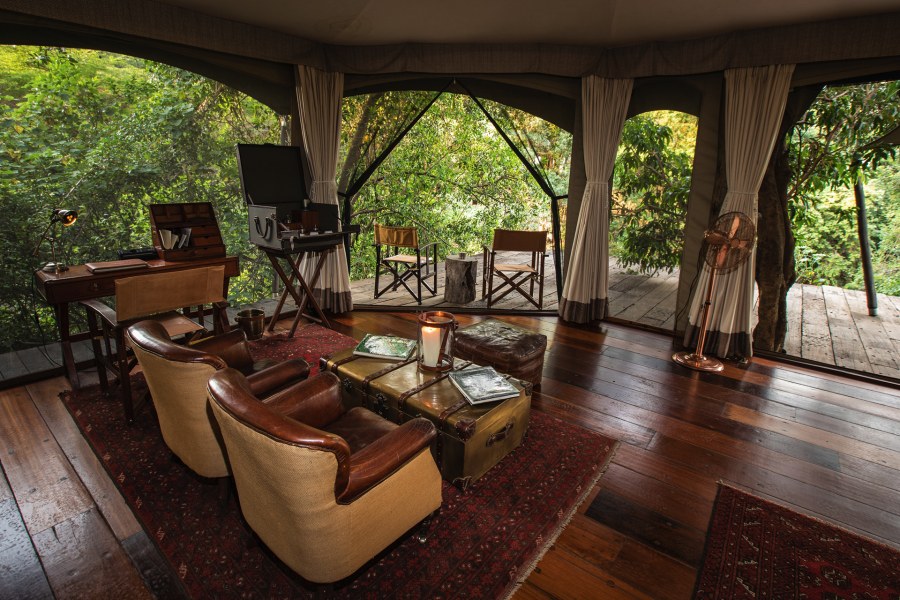 Canvas suite at Mara Plains Camp with leather armchairs, a writing desk and a deck opening into green trees