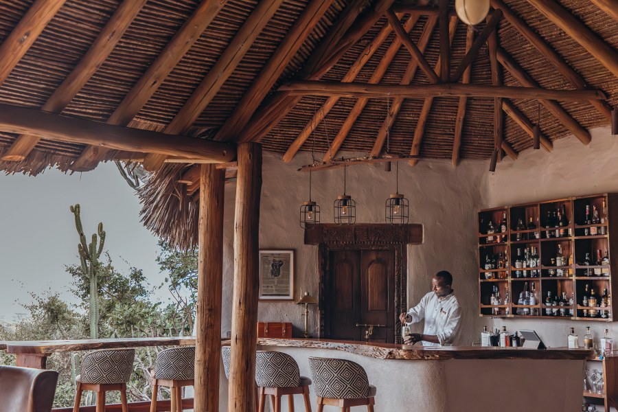 Barman pouring a drink at the thatched bar of ol Donyo Lodge, with patterned stools and a cactus outside