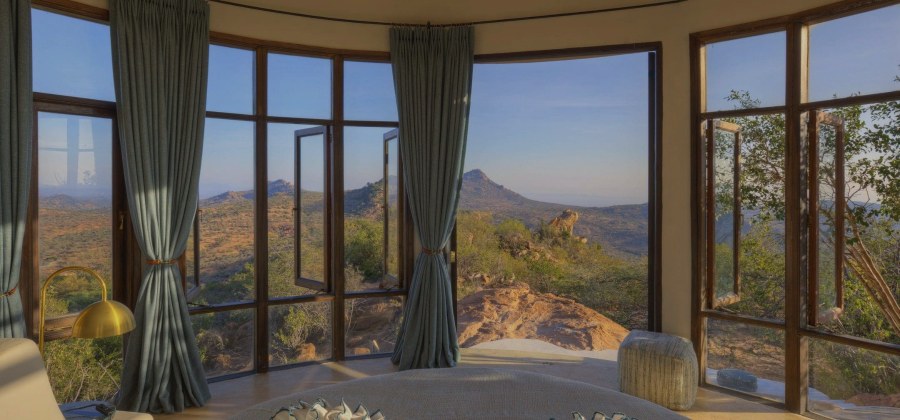 Curved wall of open windows in a villa at Ol Lentille looking out over rocky outcrops and hills in Laikipia