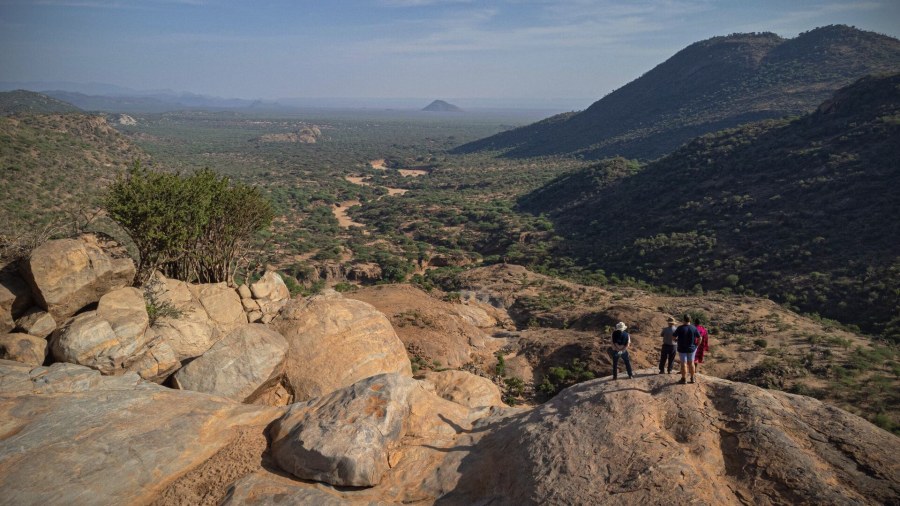 Group of walkers on large boulders above a wide valley of green bush and hills at Ol Lentille