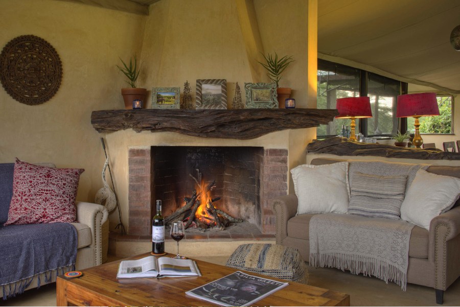 Lounge tent at Ol Pejeta Bush Camp with sofas around a lit brick fireplace and a bottle of wine on the table