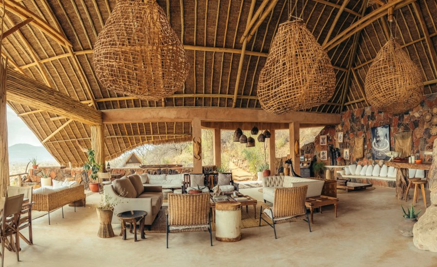 Open thatched lounge at Reteti House with woven lights, sofas, wicker chairs and a stone wall, with hills beyond