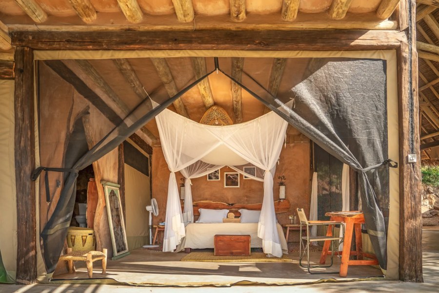 Open-fronted room at Reteti House with a bed under white netting, a wooden chest and a small desk and chair