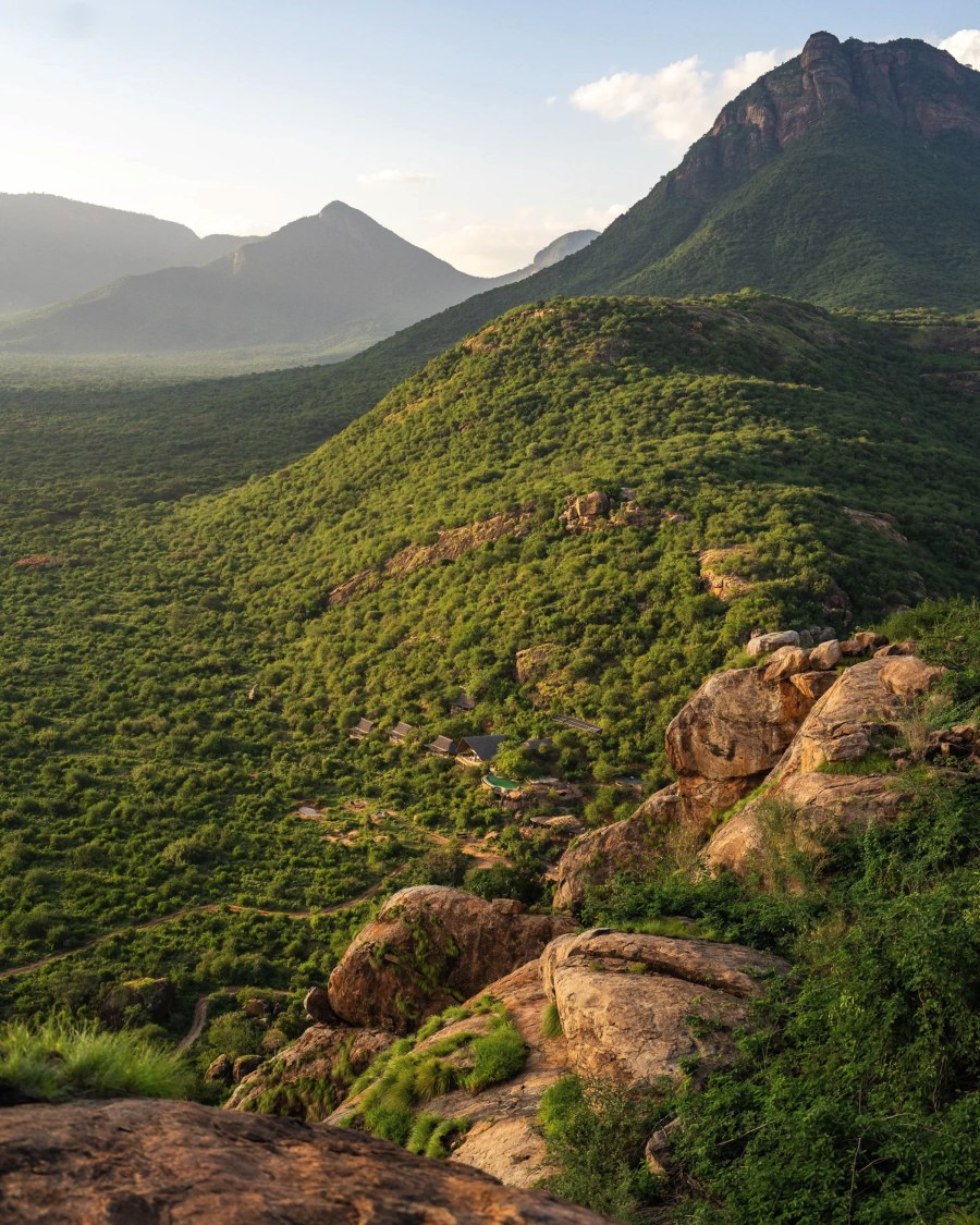 Reteti House tucked into a green, bush-covered hillside below rocky peaks in the Mathews Range, Namunyak