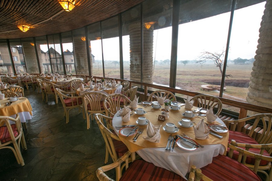 Dining room at Salt Lick Safari Lodge with set tables by tall windows looking out over a waterhole and plains