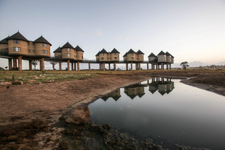 Round thatched rooms on stilts linked by walkways, reflected in a waterhole at Salt Lick Safari Lodge