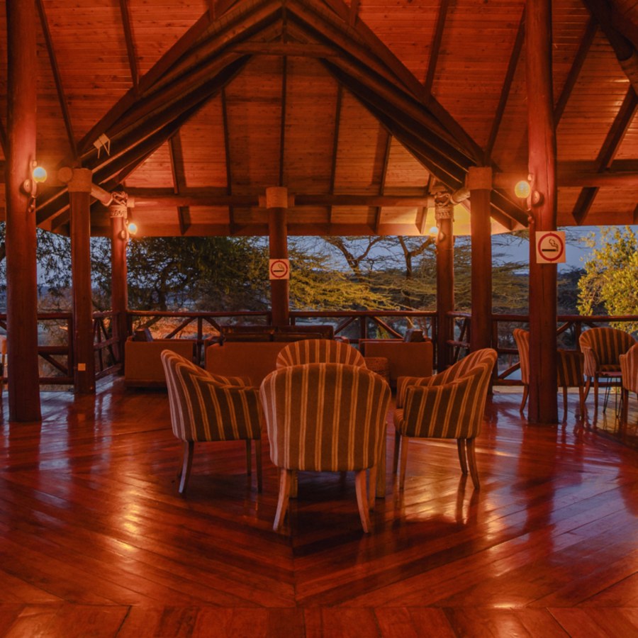 Striped armchairs on a wooden floor in an open-sided lounge with a timber roof at Samburu Simba Lodge