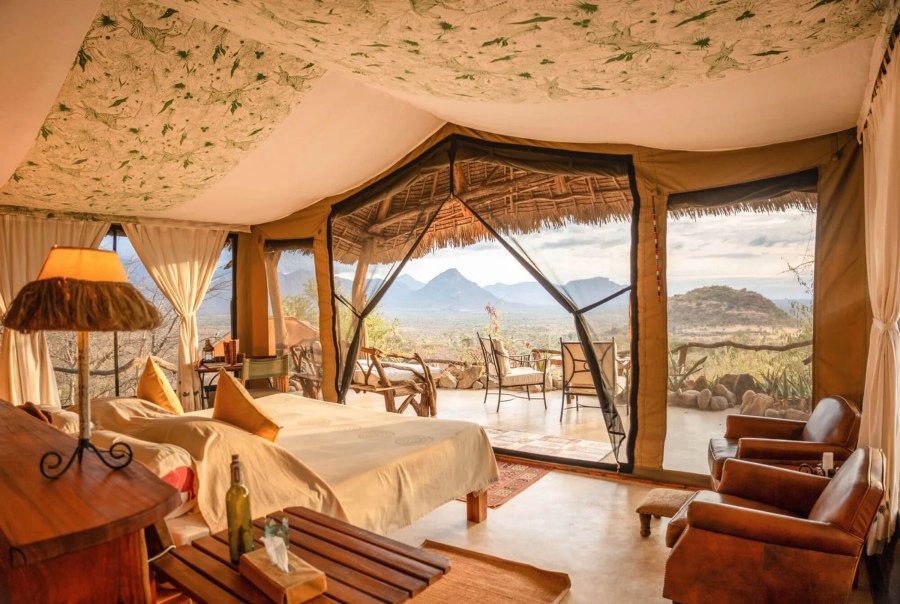 Tent bedroom with leather armchairs, opening onto a veranda with mountain views at Sarara Camp