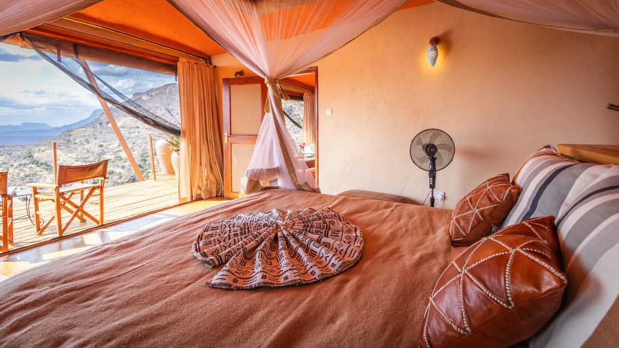 Bed with a mosquito net and leather cushions beside a deck looking over hills at Saruni Samburu