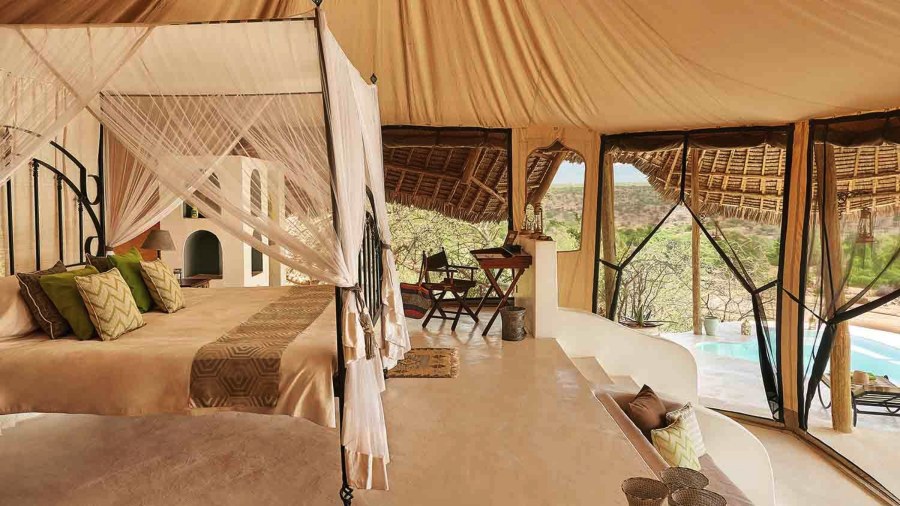Four-poster bed under a canvas roof, with a desk and a plunge pool outside at Sasaab