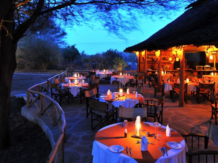 Candlelit tables on a stone terrace beside a thatched dining room at dusk at Satao Camp