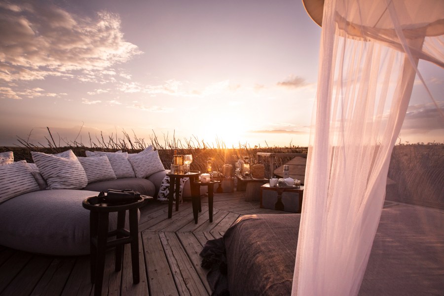 Cushioned seating and a netted bed on an open wooden deck at sunset at Segera Retreat