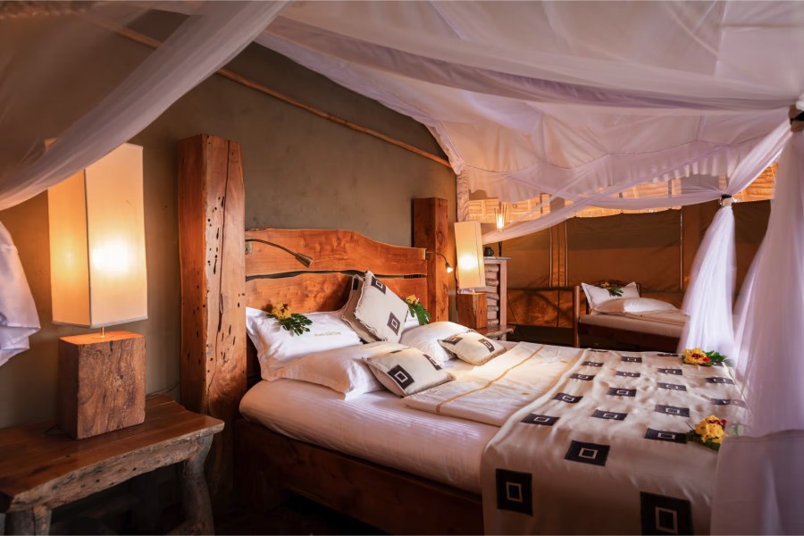 Wooden bed with a mosquito net and flower-decorated pillows inside a tent at Severin Safari Camp