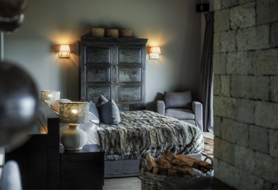 Bedroom with a fur throw on the bed, an old wooden wardrobe and a stone wall at Sirai House
