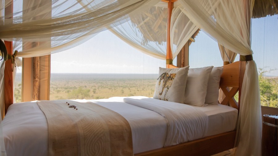 Four-poster bed with a cheetah-print cushion facing open plains at Soroi Cheetah Tented Camp