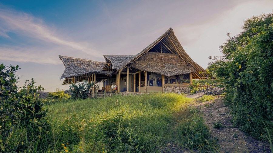 Thatched tent on a stone base at the top of a grassy rise at Soroi Cheetah Tented Camp