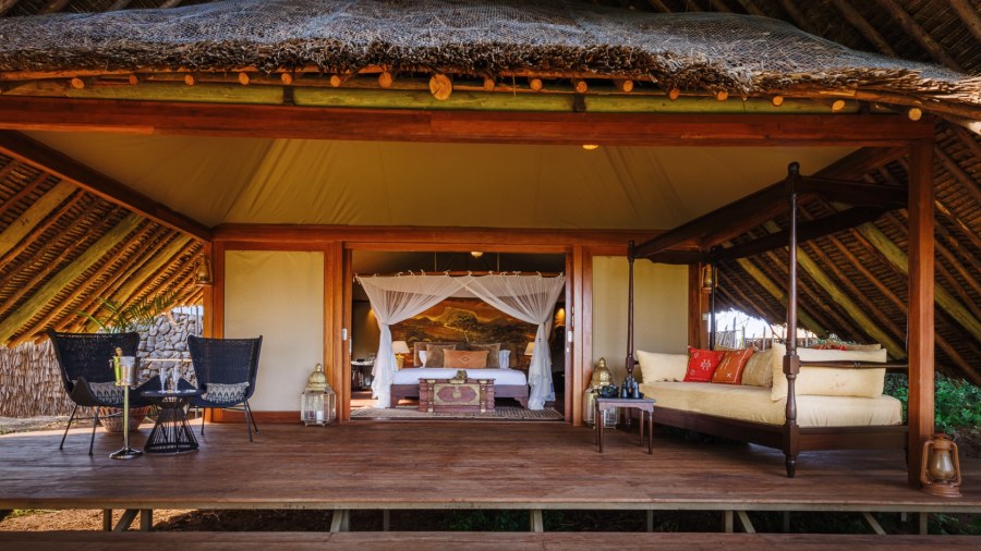 Tent veranda with a daybed and wicker chairs under a thatched roof, bedroom behind, at Soroi Larsens Camp