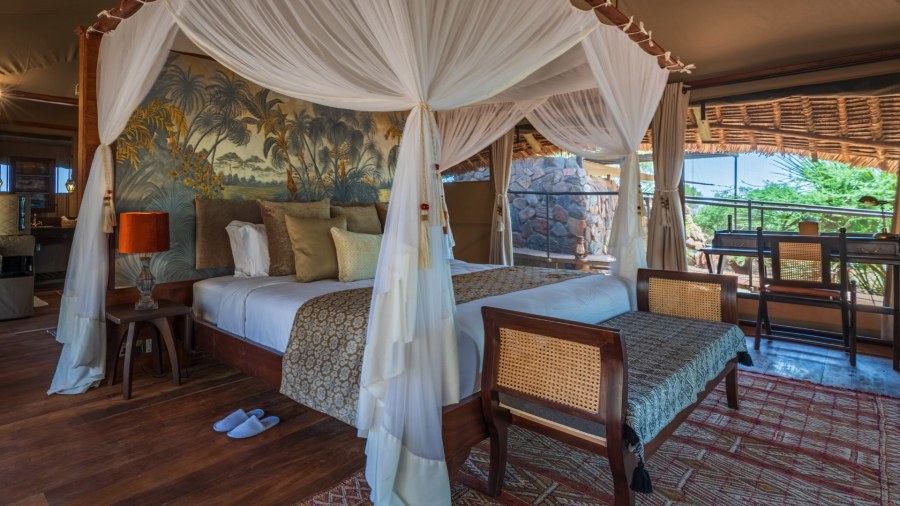 Four-poster bed with net drapes in front of a painted palm mural inside a tent at Soroi Larsens Camp