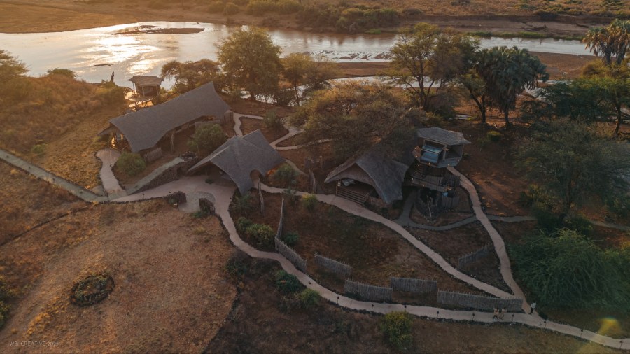 Aerial view of thatched tents linked by paths beside a wide river at Soroi Larsens Camp