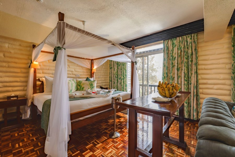 Four-poster bed with net drapes, a bowl of bananas and a balcony door at Taita Hills Safari Resort & Spa
