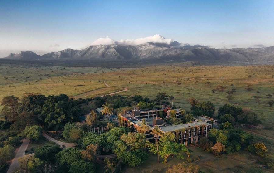 Aerial view of Taita Hills Safari Resort & Spa among trees on grassland, with a mountain range behind