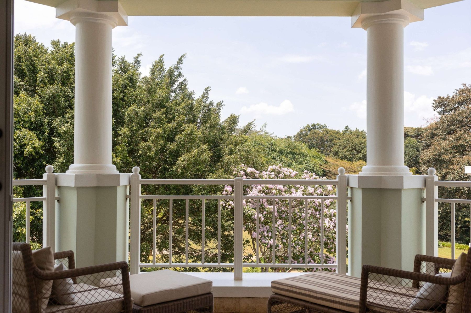 Private balcony of a suite at Hemingways Nairobi with white columns, armchairs and a view over gardens and trees