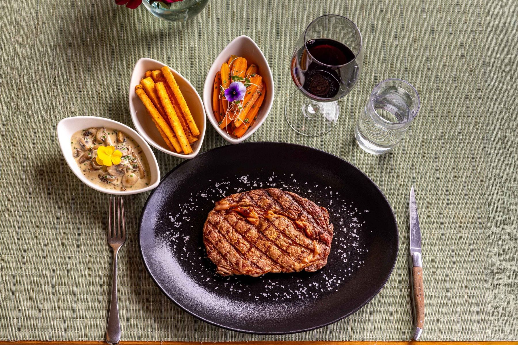 A grilled steak with side dishes and a glass of red wine on a table at Hemingways Nairobi