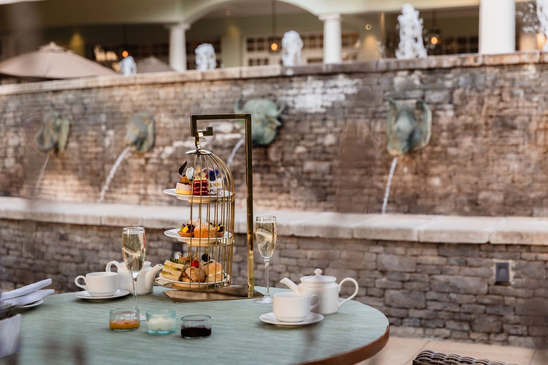 Afternoon tea on a cake stand with tea and champagne, beside a stone wall with fountains at Hemingways Nairobi