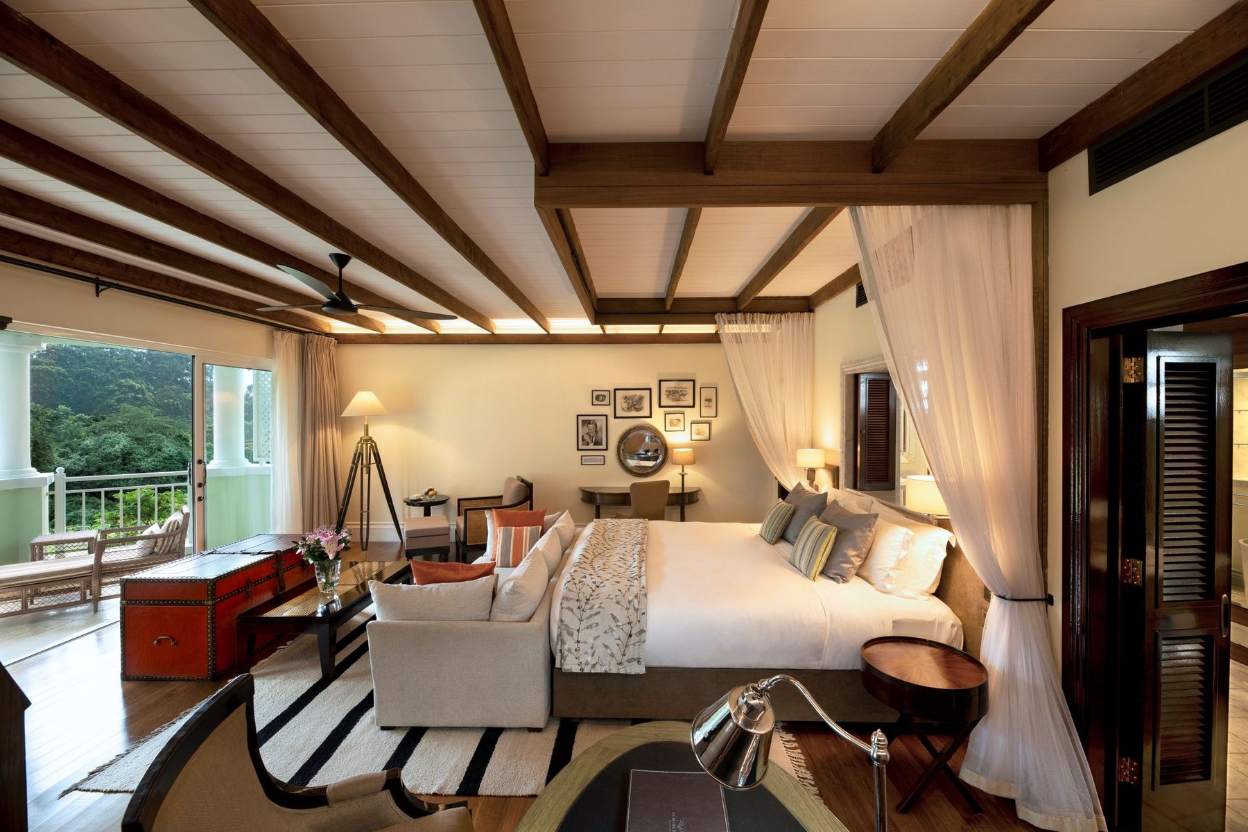 Suite at Hemingways Nairobi with a canopy bed, beamed ceiling, sofa and a window onto green hills