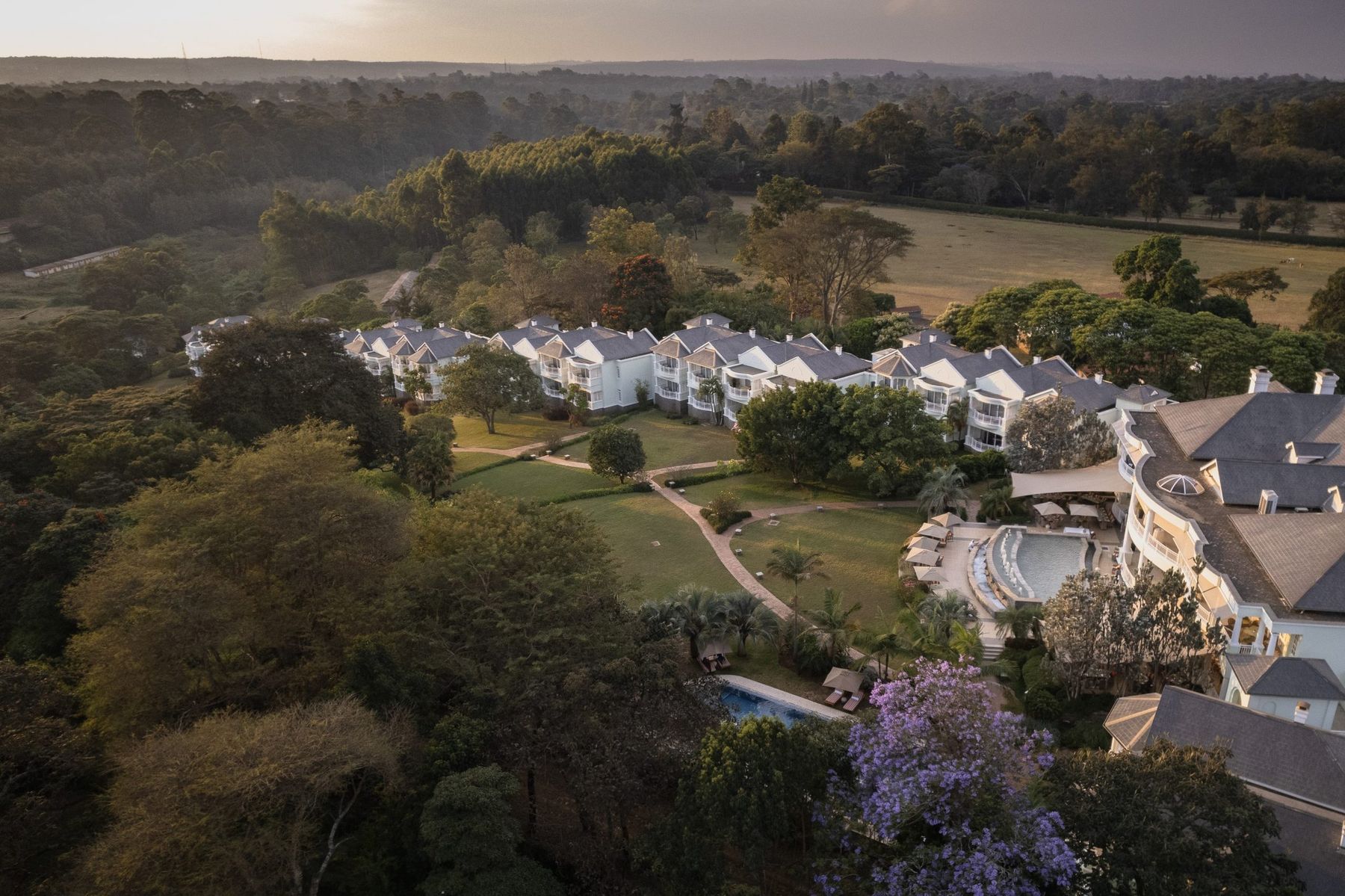 Aerial view of Hemingways Nairobi, white buildings among lawns and tall trees in Karen at sunrise