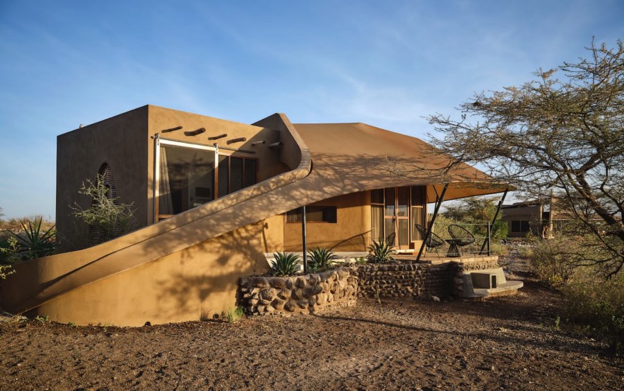 Earth-coloured building with a curved canvas roof and stone terrace among acacias in Buffalo Springs National Reserve