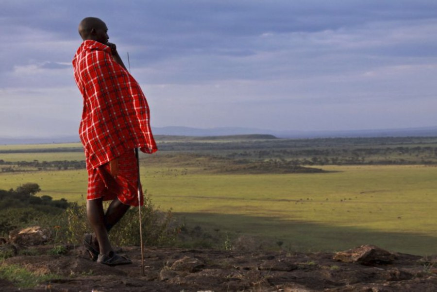 Maasai man in a red shuka looking out over open plains from a rocky rise in Olare Motorogi