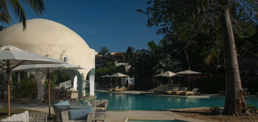 Pool with sun loungers, umbrellas and a white domed building at Swahili Beach Resort in Diani