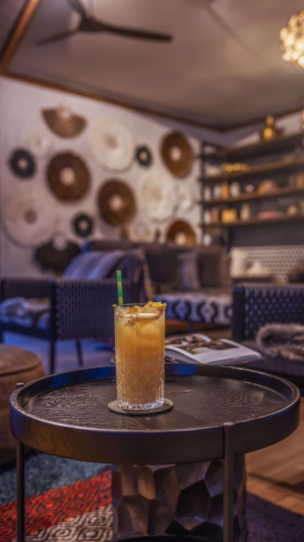 Cocktail on a round table in the bar at JW Marriott Masai Mara Lodge, with sofas and a wall of woven discs